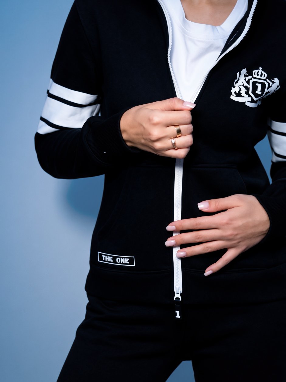 69 black jumpsuit close-up: embroidered crest and white zipper | THE ONE