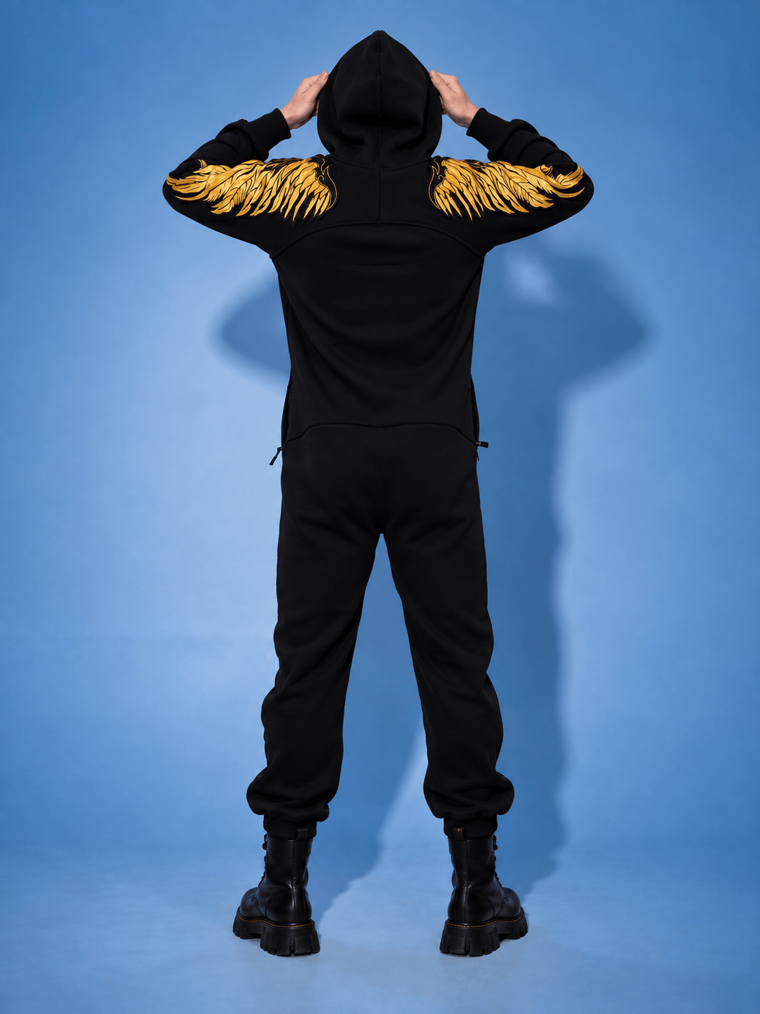 Angel black jumpsuit with hood up, back view: gold wings across the arms | THE ONE